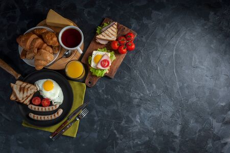 Fried eggs, sausages and vegetables on pan. Delicious breakfast with orange juise and croissant on wooden rustic boards, food background.の写真素材