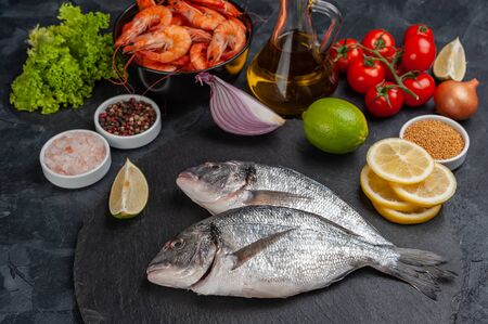Fresh dorado fishes and shrimps on bord prepared to cooking, vegetables and fresh sea food. Cooking background, selective focusの写真素材