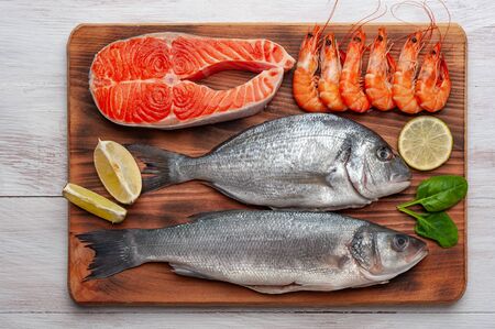 Fresh dorado, seabass, salmon fishes and shrimps on bord prepared to cooking, vegetables and fresh sea food. Cooking background, flat layの写真素材