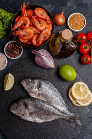 Fresh dorado fishes and shrimps on bord prepared to cooking, vegetables and fresh sea food. Cooking background, flat layの写真素材