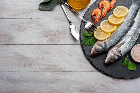 Fresh seabass fishes and shrimps on bord prepared to cooking, vegetables and fresh sea food. Cooking background, flat layの写真素材