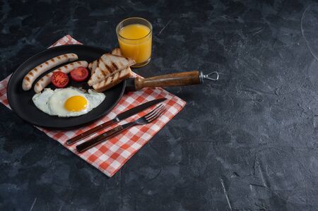 Fried eggs with sausage and vegetables on pan. Breakfast with orange juise and croissant on wooden rustic boards, food background.の写真素材