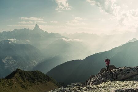 Mountaineer with backpack on rock enjoying view of big mountains, hiking lifestyle, man on top. Retro film filter, vintage stylizationの写真素材