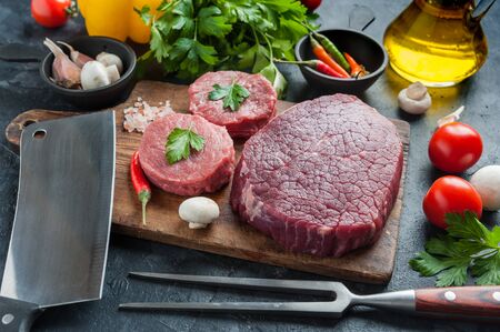Beef steaks ready to cooking on culinary background and vegetables. Fresh raw meat on wooden cutting board with rosemary, selective focusの写真素材