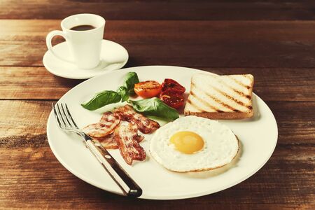Fried eggs with bacon and vegetables, breakfast on wooden rustic boards, food background. Retro film filter, vintag stylizationの写真素材