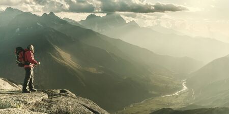 Mountaineer with backpack on rock enjoying view of big mountains, hiking lifestyle, man on top. Vintage stylization, retro film filterの写真素材