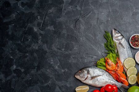 Fresh dorado, seabass fishes and shrimp on bord prepared to cooking, vegetables and fresh sea food. Cooking background, flat layの写真素材
