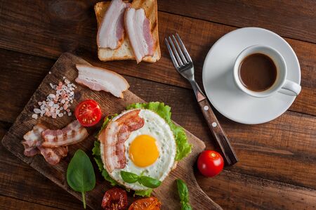 Breakfast with fried egg and bacon on sandwich and coffee on wooden table. Morning food, flat layの写真素材
