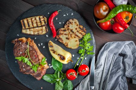 Beef steaks rib eye and vegetables fried on grille, culinary background. Grilled meat on cutting board with spice, flat layの写真素材