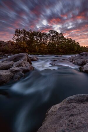 Fall landscape with river on sunrise and bright autumn trees under colorful sky, long exposureの写真素材