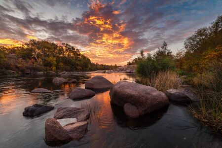 Fall landscape with river on sunrise and bright autumn trees under colorful sky, long exposureの写真素材
