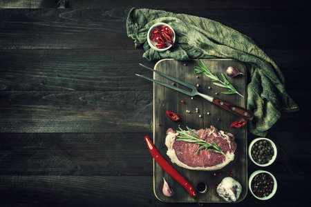 Beef steaks rib eye ready to cooking, culinary background. Fresh raw meat on wooden cutting board with rosemary, flat lay. Vintage stylization, retro film filterの写真素材