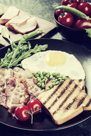 Fried eggs with bacon and vegetables, breakfast on wooden rustic boards, food background. Vintage stylization, retro film filterの写真素材
