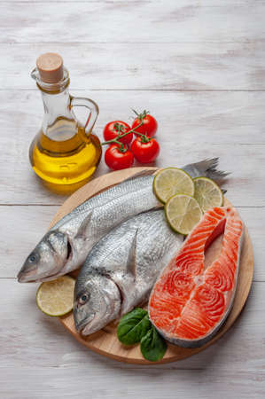 Fresh dorado, seabass and salmon fishes on bord prepared to cooking, vegetables and fresh sea food. Cooking background, flat layの写真素材
