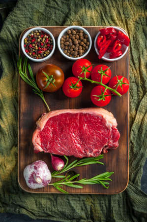 Fresh raw beef steaks rib eye ready to cooking, culinary background. Meat on wooden cutting board with rosemary, flat layの写真素材