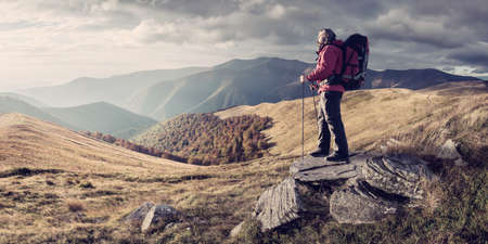 Mountaineer with backpack on rock enjoying view of big mountains, hiking lifestyle, man on top. Retro film filter, vintage stylizationの写真素材