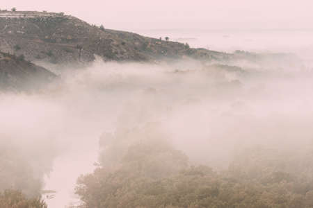 Autumn landscape with fog in valley above river, foggy morning. Vintage stylization, retro film filterの写真素材