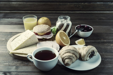 Breakfast with tea, orange juise and croissant on wooden rustic boards. Food background, copy space. Retro stylization, vintage film filterの写真素材