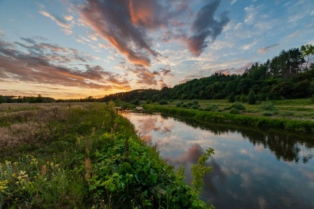 Summer landscape with river and meadow and majestic sunset with bright clouds in skyの写真素材