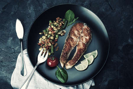 Fried salmon fishes and vegetables on plate, cooking delicious and healthy, fresh sea food. Cooking background, flat lay. Retro stylization, vintage film filterの写真素材