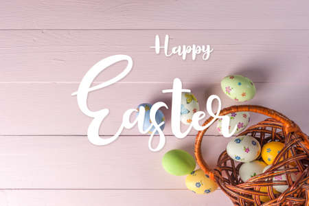Happy easter painted eggs in basket on wooden table and hand lettering textの写真素材