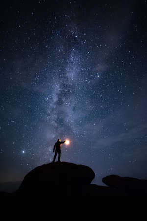 Night landscape with man keeps lantern on mountains peak and stars in beautiful skyの写真素材
