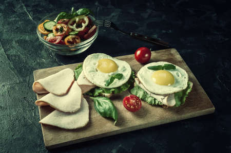 Fried eggs with bacon and vegetables, breakfast on wooden rustic boards, food background. Retro stylization, vintage film filterの写真素材