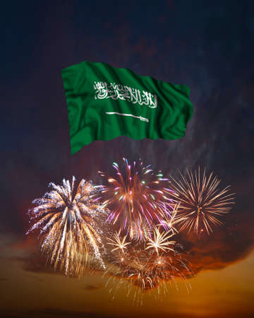 Holiday fireworks in evening sky and flag of Saudi Arabia for National Independence dayの写真素材