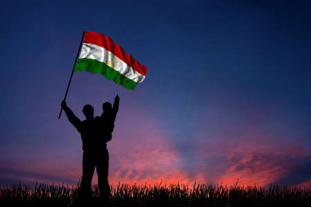 Father and son hold the flag of Tajikistan against backdrop of a beautiful sunset skyの写真素材