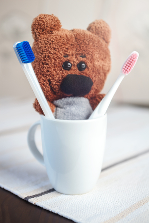 Handmade Teddy Bear with Red and Blue Plastic Toothbrushes in White Mug on Blurred Background Concept Dentalの写真素材