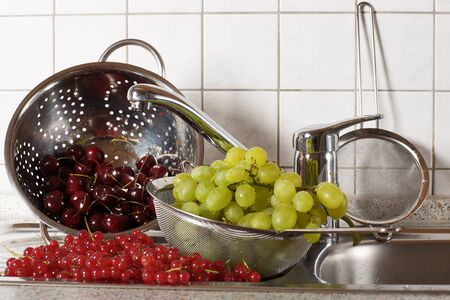 Fresh fruits and berries being washed in a strainerの写真素材