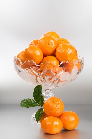 Crystal glass footed bowl of orange mandarins on silver backgroundの写真素材