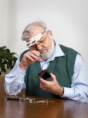 Senior man watching his new smart phone under loupeの写真素材