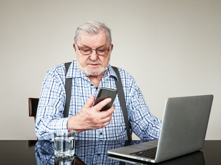 Portrait of active senior man with laptop and smart phone at home. Old man using computer sitting...