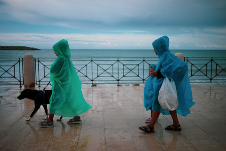 Two colorful people walking in the rain in front of the seaのeditorial素材
