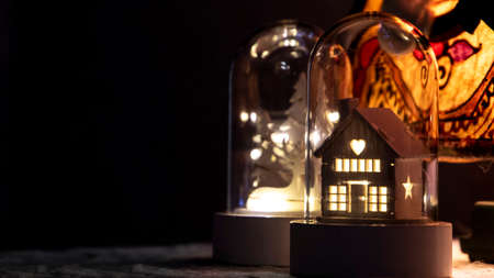Little wooden house with warm lights inside a glass bell. Christmas decoration. Dark Background.の写真素材