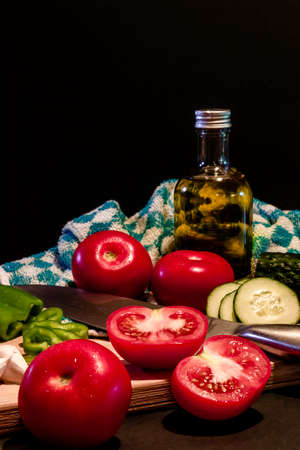 Close up of traditional summer cold tomato soup gazpacho ingredients on a wood plank -Tomatoes, pepper, cucumber, garlic and olive oil - black background - mediterranean, spanish food conceptの写真素材