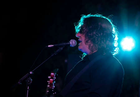 Man singing and playing bass on stage with backlit bright blue lights - live music event conceptの写真素材