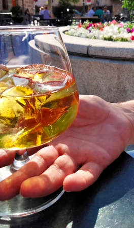 close-up of one hand taking a glass of whiskey on the rocks in a table of a terrace bar on a sunny day. Break time conceptの写真素材