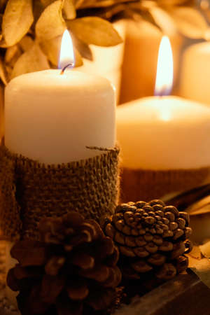 Close up of two burning candles with burlap decoration and two pine cones. Warm interior. Selective...