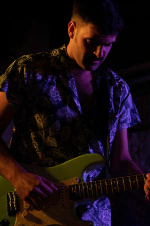 young musician playing guitar on a stage during a concert by night