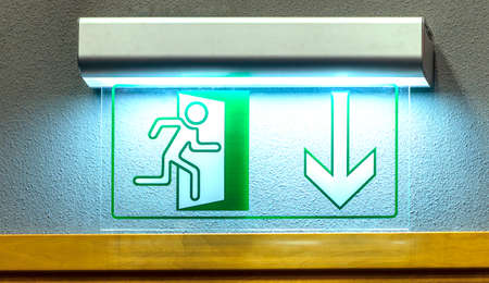 Illuminated green emergency exit light sign on the wall. close-up