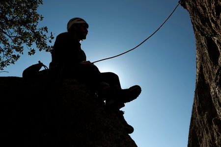 Silhouette of a rock climber sitting on a ledge while supporting his teammate in Torrelodones,...