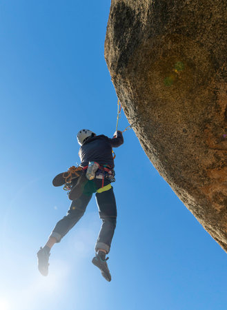 young adult hanging from a granite overhang. Rock climbing. Extreme sports concept