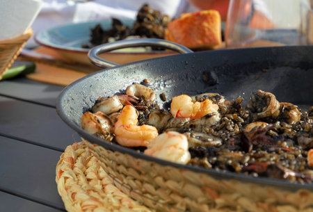 Black rice with squid and shrimp in a paella pan. Ready to eat, with bread and red wineの写真素材