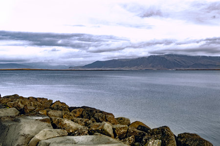 Scenic view of stone fence on highland overlooking calm rippling seawater and with rocky mountain...