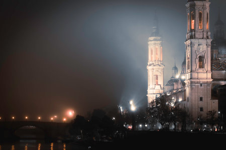 Exterior of famous Cathedral Basilica of Our Lady of the Pillar surrounded by trees and glowing streetlamps at dusk in Spainの写真素材