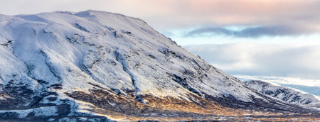 Majestic view of mountain range covered with ice in desert during summertime under cloudy sky at sundownの写真素材