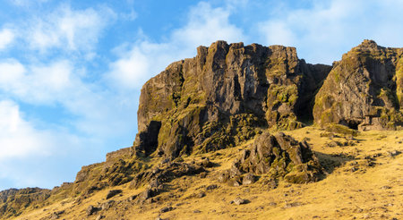A rocky hillside with a cloudy sky in the background. The sky is blue and the hill is covered in rocksの写真素材