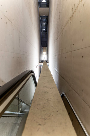 A long, narrow hallway with a concrete wall. The wall is covered in small holes and has a gray...